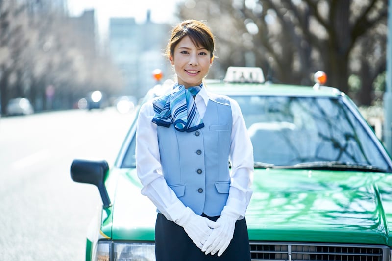 Female taxi driver standing in front of a taxi