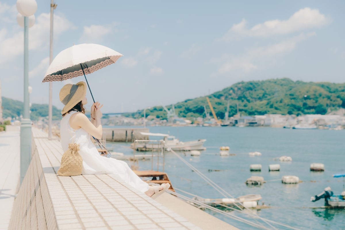 Woman holding sun umbrella while looking out onto a bay