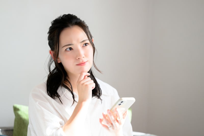 Woman looking thoughtful while using her smartphone (Japanese phone number article)