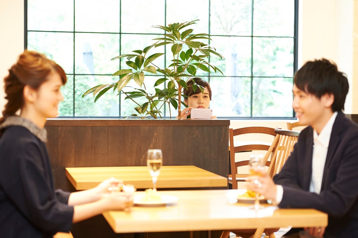 Woman surreptitiously taking smartphone photo of a man dining with another woman
