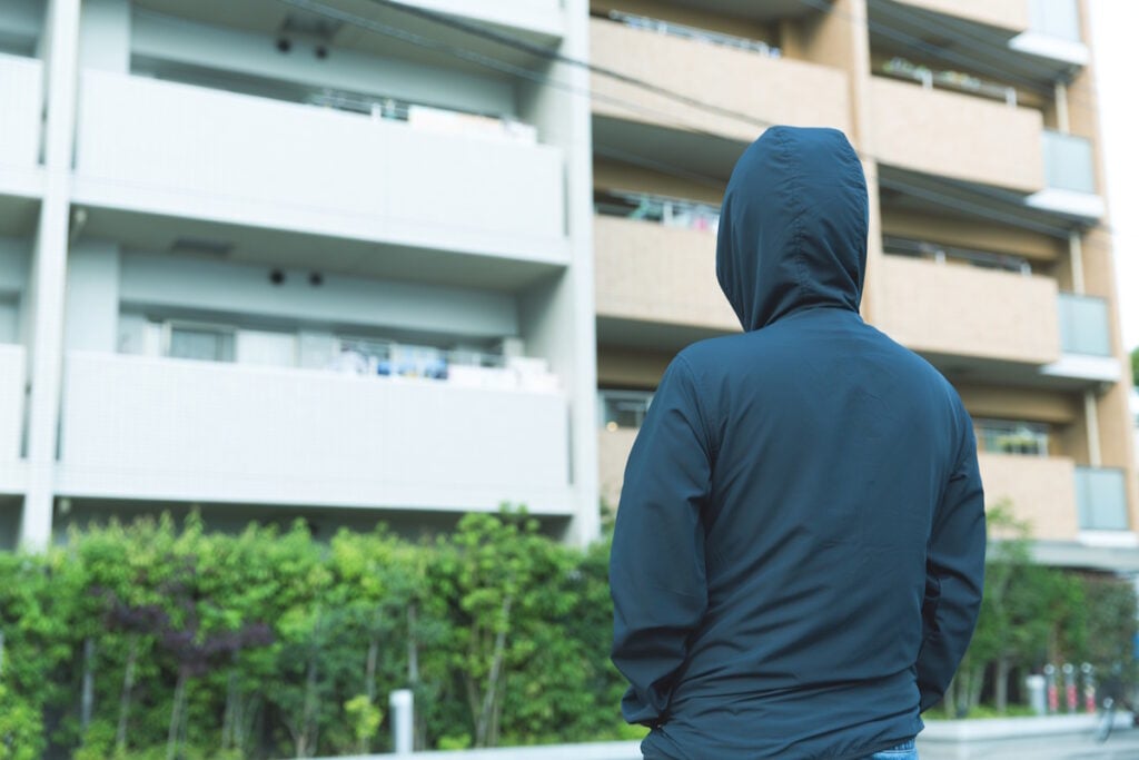 Man in hoodie looking creepily at an apartment building