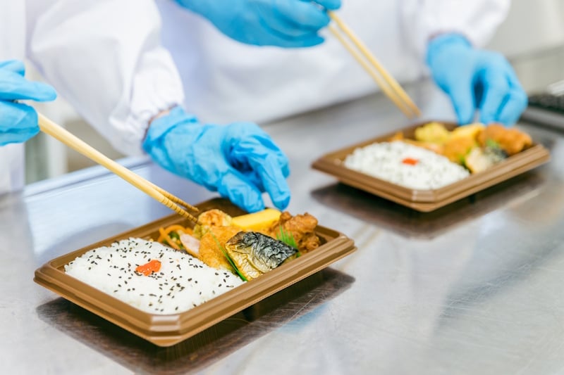 Women wearing blue gloves and preparing bento lunches with kitchen chopsticks