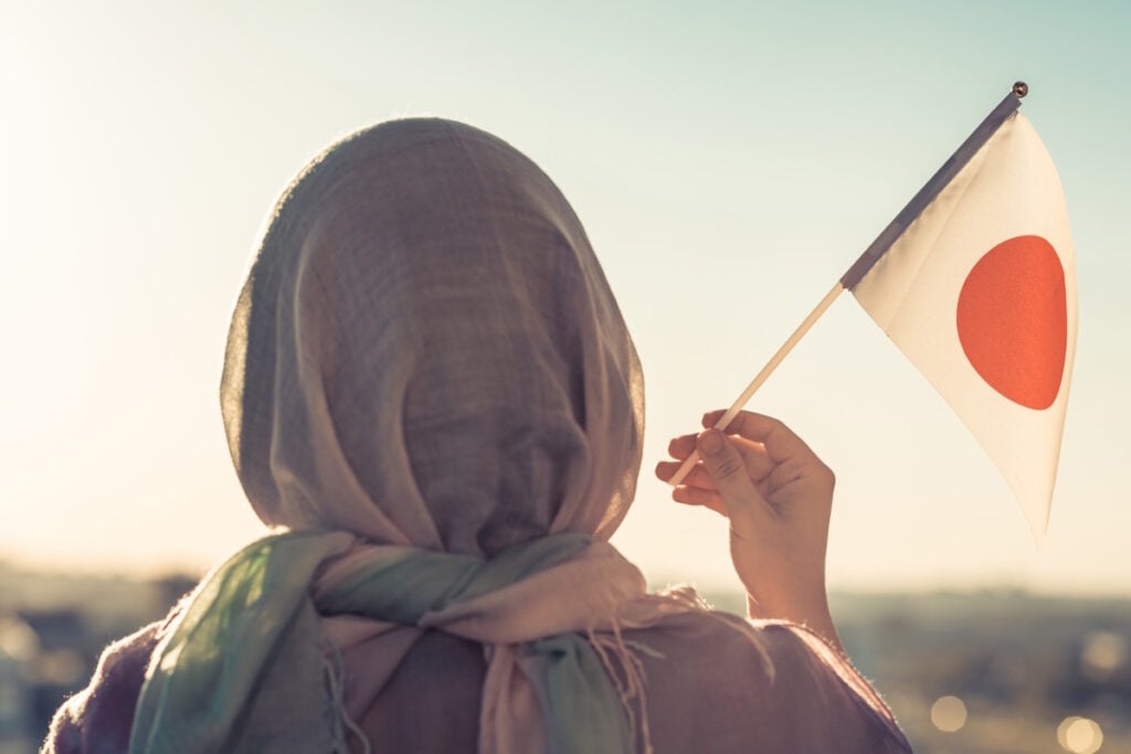 Muslim woman in scarf with Japanese flag at sunset