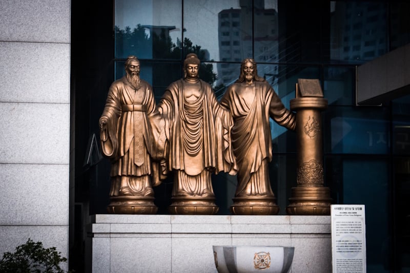 A statue in front of Unification CHurch headquaretrs in Seoul, South Korea, depicting Confucius, the Buddha, Jesus Christ, and the Quran. 