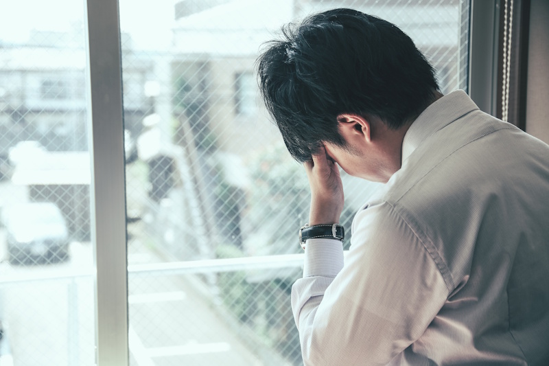 Man looking out a window and holding his head as if stressed