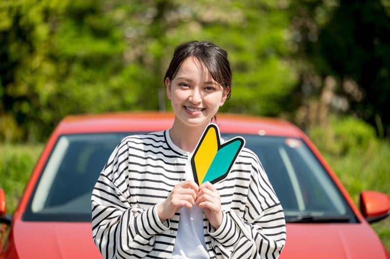 New driver in Japan holding a yellow and green "beginner driver's" sticker that must be displayed in the car for a year. 