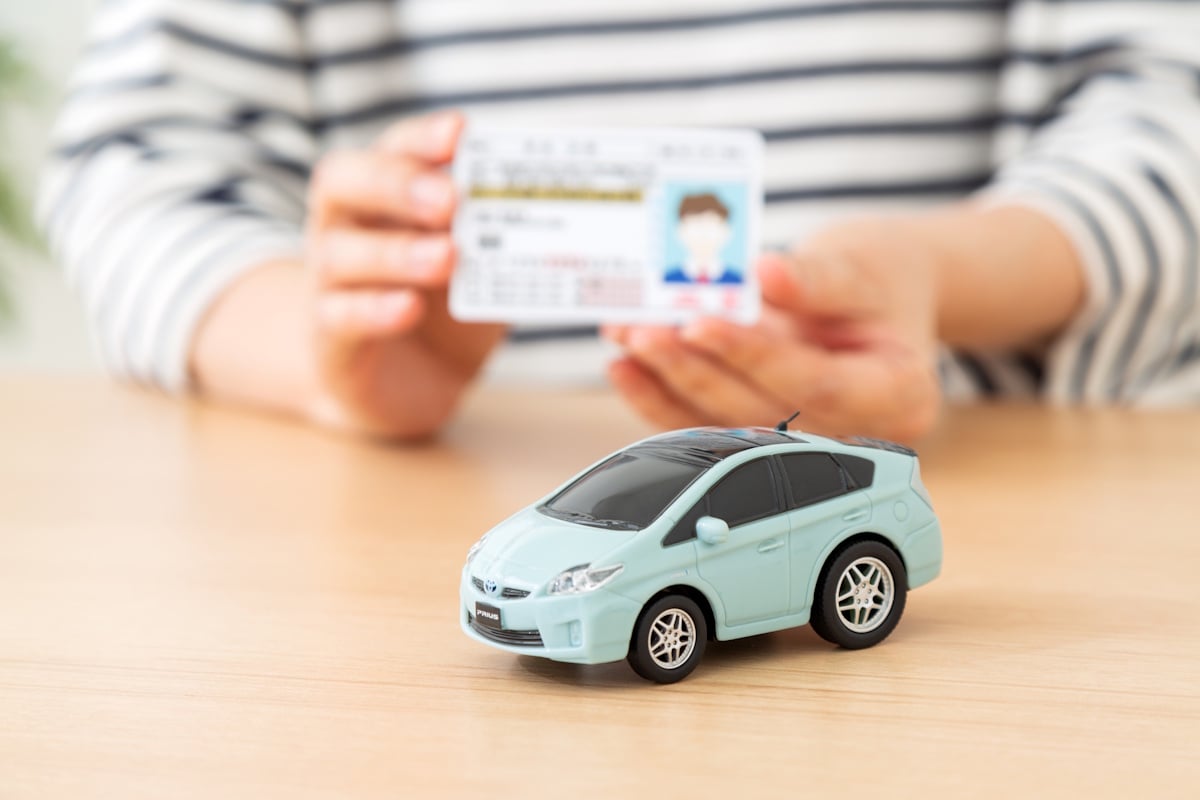 Woman holding fake Japanese driver's license behind a toy car