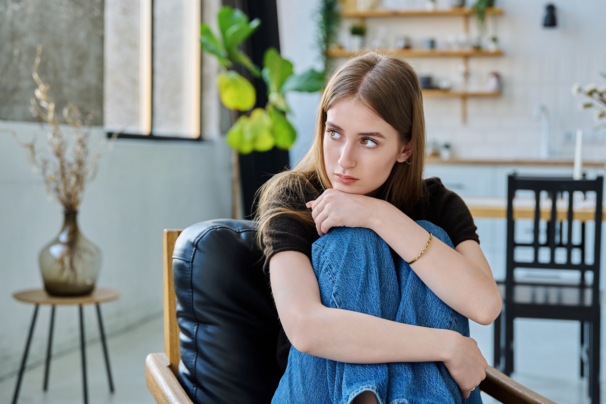 Sad unhappy thoughtful serious young woman sitting in armchair at home