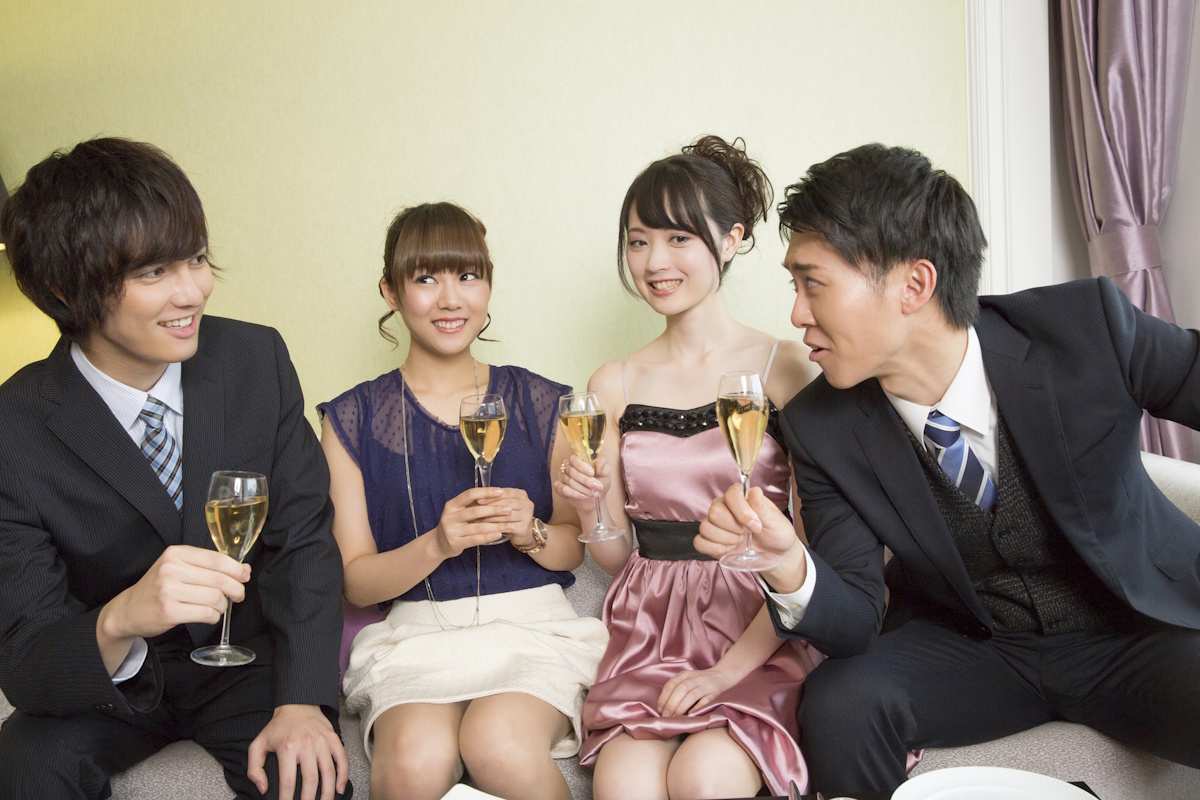 Two men and two women in formal dress holding champagne glasses and talking. The men are talking past the women, who look like they're being paid to smile