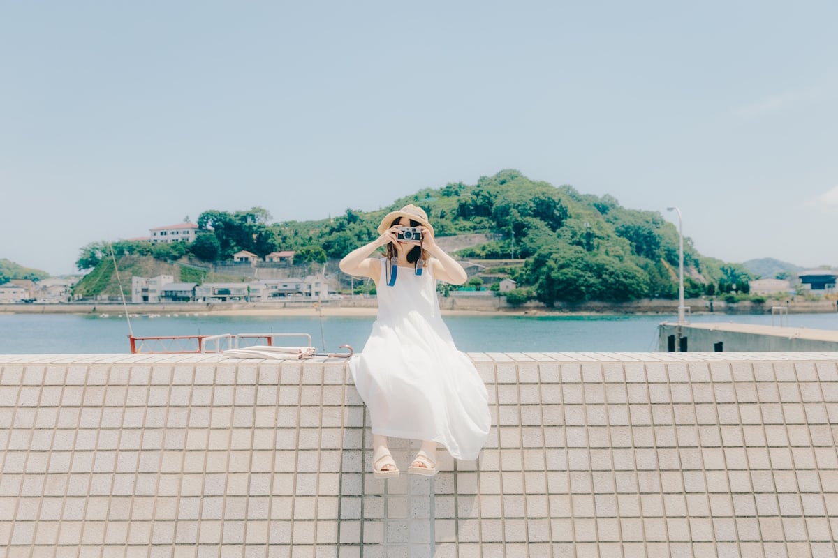 Woman sitting on wall holding up a camera to her face