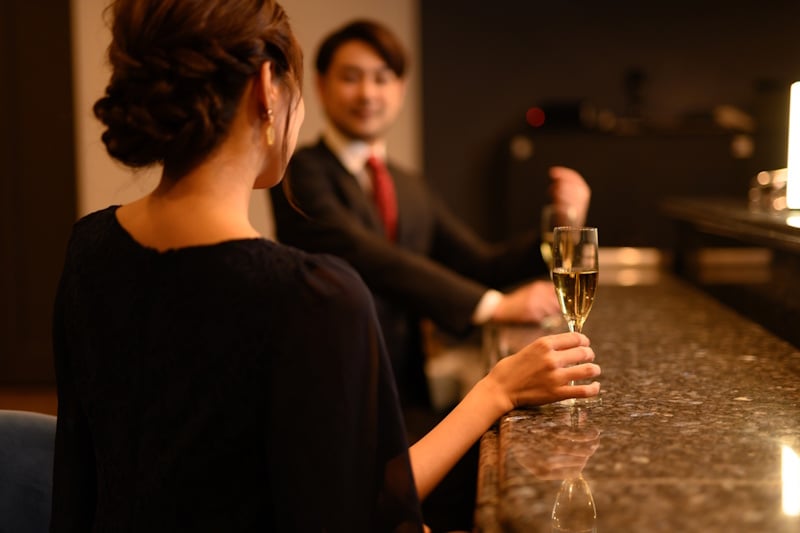 Woman holding a champagne glass and looking at man across the room in a bar