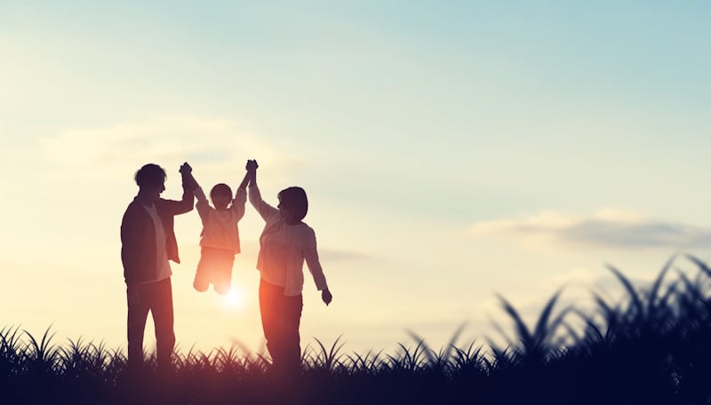 Parents holding child aloft in the air by the arms with a sunset in the background