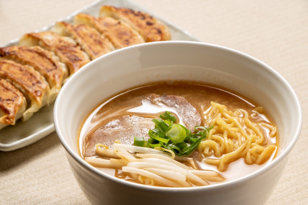 Bowl of ramen with gyoza behind it on a separate platter
