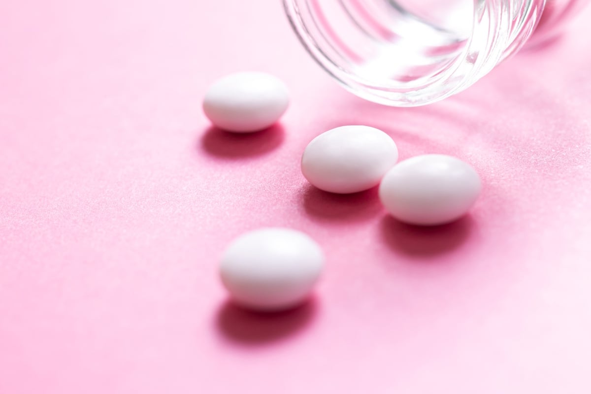 Pills tumbling out of a glass against a pink background