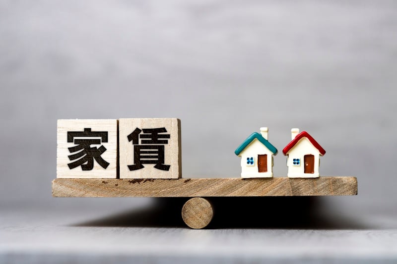 Picture of the Japanese word for rent (yachin) balanced on a teeter totter across from a set of houses