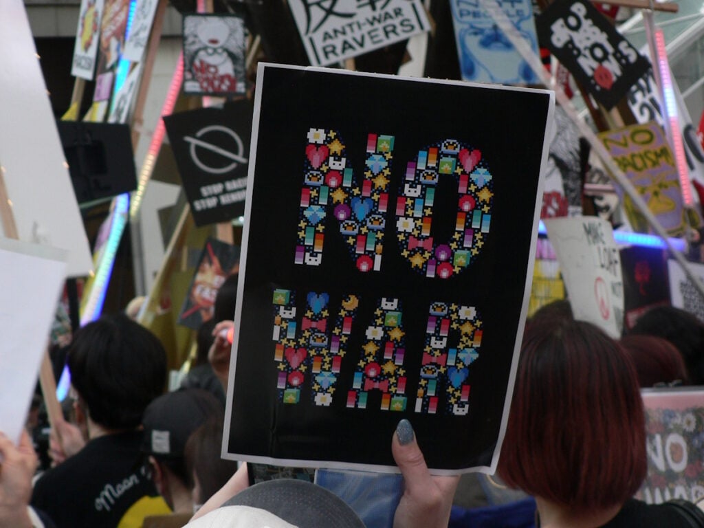 A protestor at the March 29th protest rave in Shinjuku,Tokyo against the Iran War holds up a "NO WAR" sign