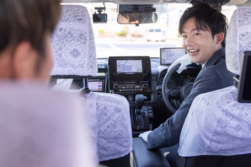 Japanese taxi driver in white gloves smiling at a passenger from the driver's seat