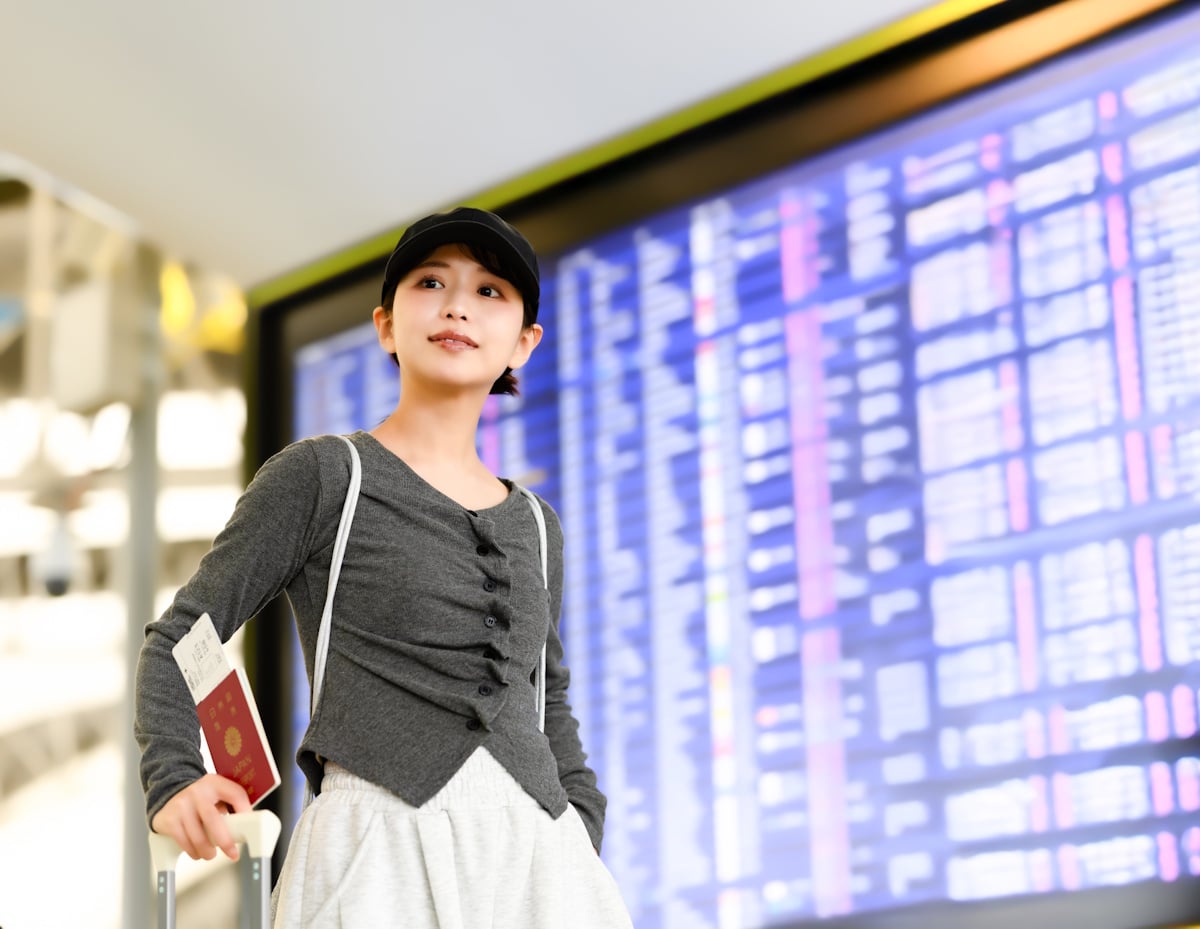 Woman at the airport standing with her passport in front of a departures board