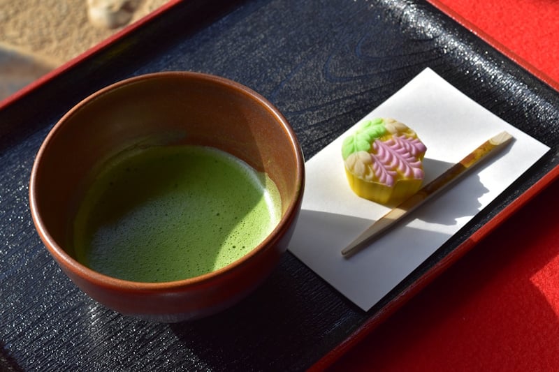 A bowl of whisked matcha served alongside a leaf-shaped wagashi sweet on a wooden tray