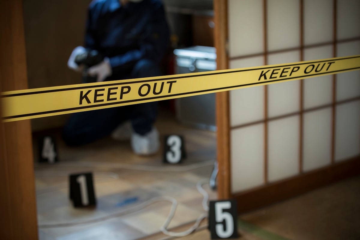 Forensic examiner takes pictures of a crime scene. Yellow KEEP OUT tape can be seen in the foreground